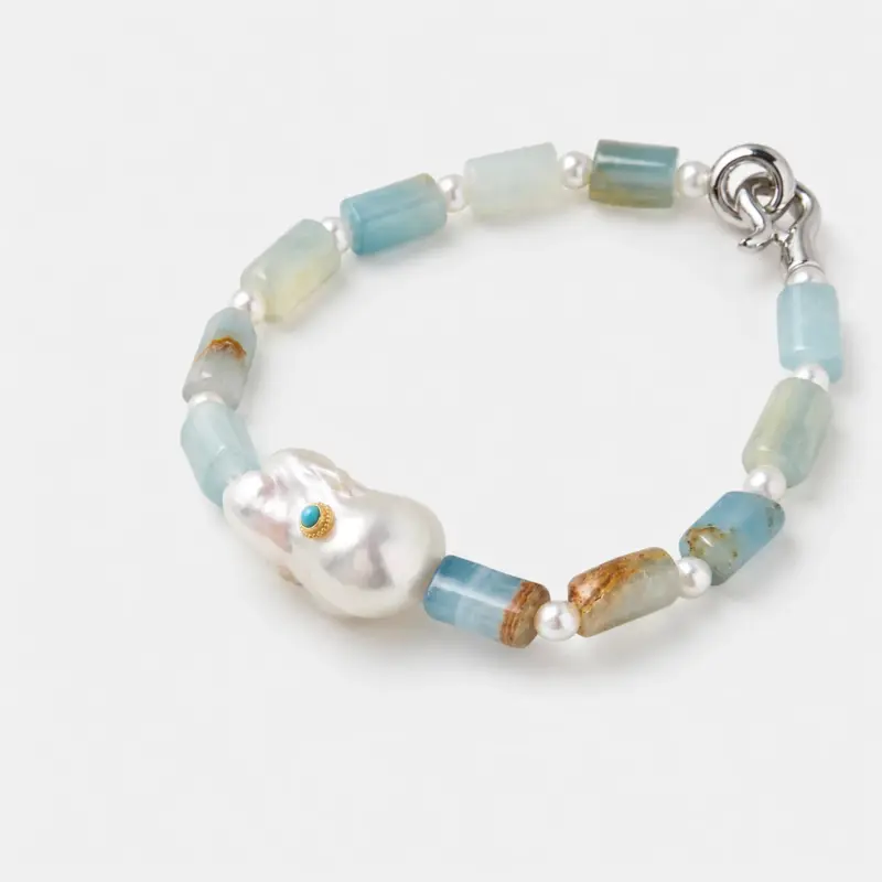 Angled detail view showing the soft blue Peruvian opal beads and an irregular large central baroque pearl with a tiny bezel-set turquoise accent stone.