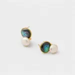 Angled detail view showing the shifting blue-green light of the circular abalone shell and white pearl stud earrings finished with polished 18K gold plated rims.