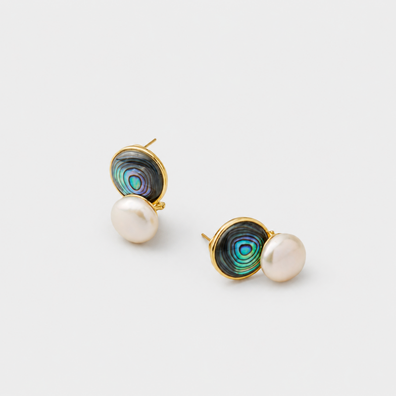 Angled detail view showing the shifting blue-green light of the circular abalone shell and white pearl stud earrings finished with polished 18K gold plated rims.