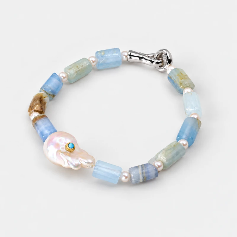 Angled view of an ONDA LENTA beaded bracelet featuring blue-green gemstones, freshwater pearls, a baroque pearl centerpiece and silver-tone clasp.