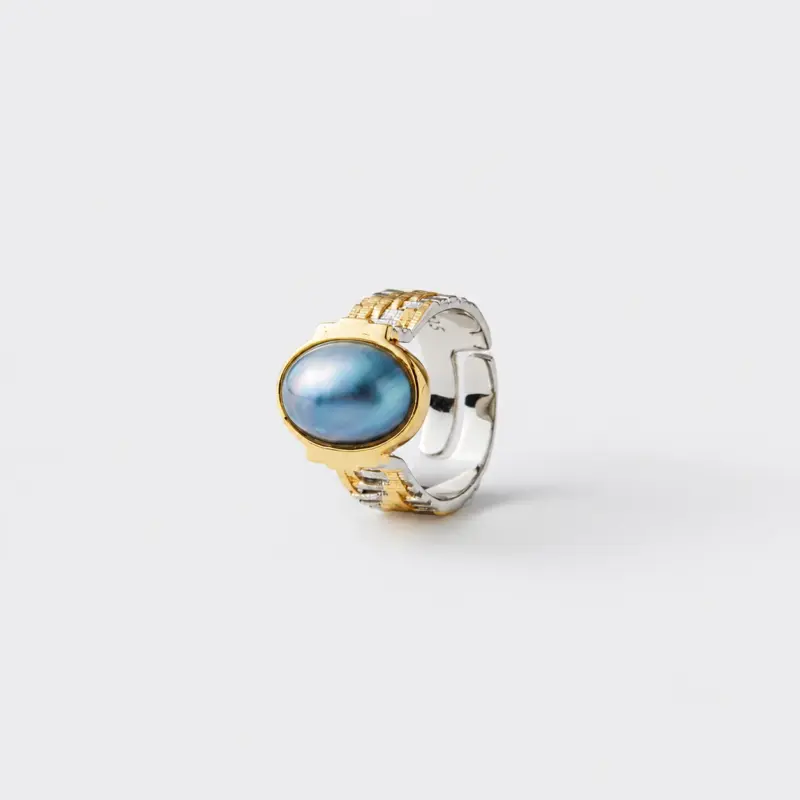 Close-up detailed view showcasing the ocean-like glow of the blue mabe pearl and the intricate mixed-metal ridges of the statement ring band crafted with 18K gold plating and sterling silver