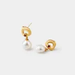 Close-up detailed view of the brushed matte texture and inset red garnet within the hollow top of pearl drop earrings crafted in 18K gold plated silver