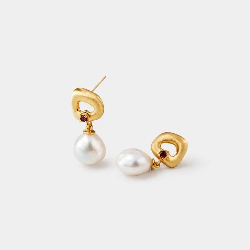 Close-up detailed view of the brushed matte texture and inset red garnet within the hollow top of pearl drop earrings crafted in 18K gold plated silver