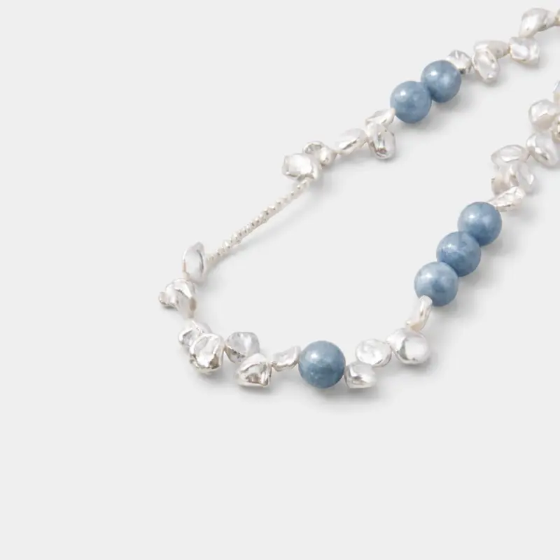 Close-up detail view showcasing the hazy matte texture and misty cloud inclusions of round blue chalcedony beads layered with organic petal-shaped baroque pearls on a sterling silver wire