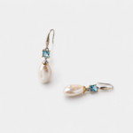 Close-up detailed view of the square-cut blue topaz stones and shell-shaped two-tone metal elements above naturally irregular baroque pearl drop earrings crafted in 18K gold plated sterling silver