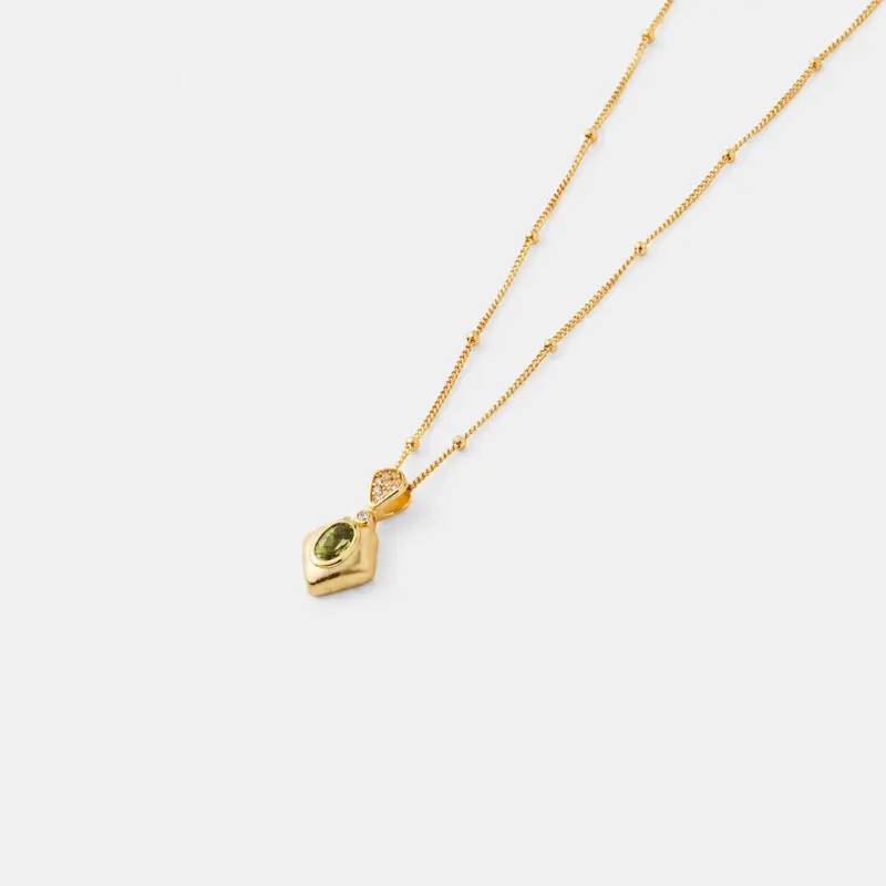 Close-up detail view focusing on the prong-set faceted green peridot stone within the diamond-shaped pendant on an 18K gold plated sterling silver chain