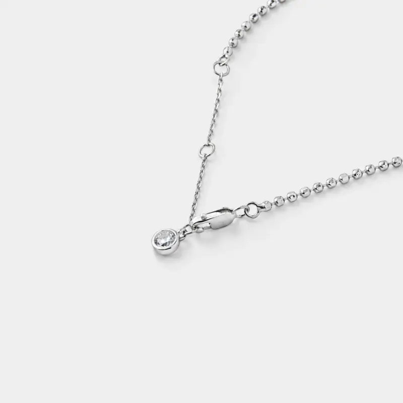 Close-up detail view of the shimmering silver-white zircon charm and fine bead links on this delicate chain bracelet crafted in rhodium plated sterling silver