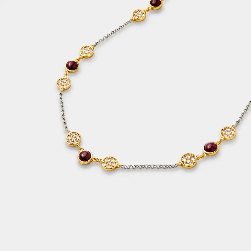 Close-up view showing the detailed cubic zirconia pavé blossom frames and smooth ruby beads on a two-tone silver and gold chain.