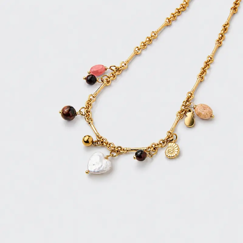 Close-up perspective view showing a heart-shaped shell pendant and dangling gemstone charms on an 18K gold-plated necklace.