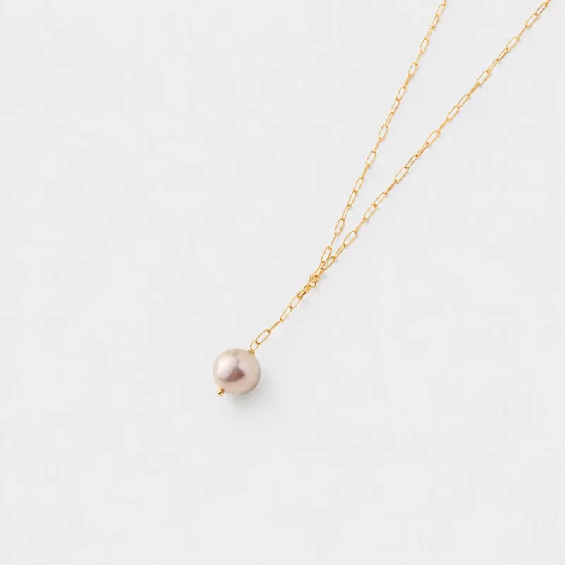 Close-up view showing a pink pearl charm and elongated links on a drop necklace with 14K gold-filled hardware.
