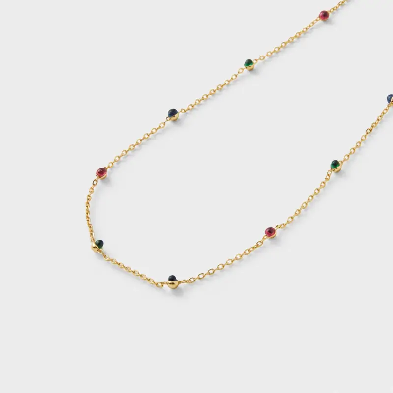 Close-up view showing red, green, and deep blue corundum accents spaced along a fine gold chain necklace in 18K gold plated silver.
