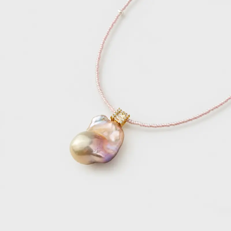 Close-up perspective view showing a square gold clasp and a baroque pearl pendant necklace with 14K gold-filled accents.