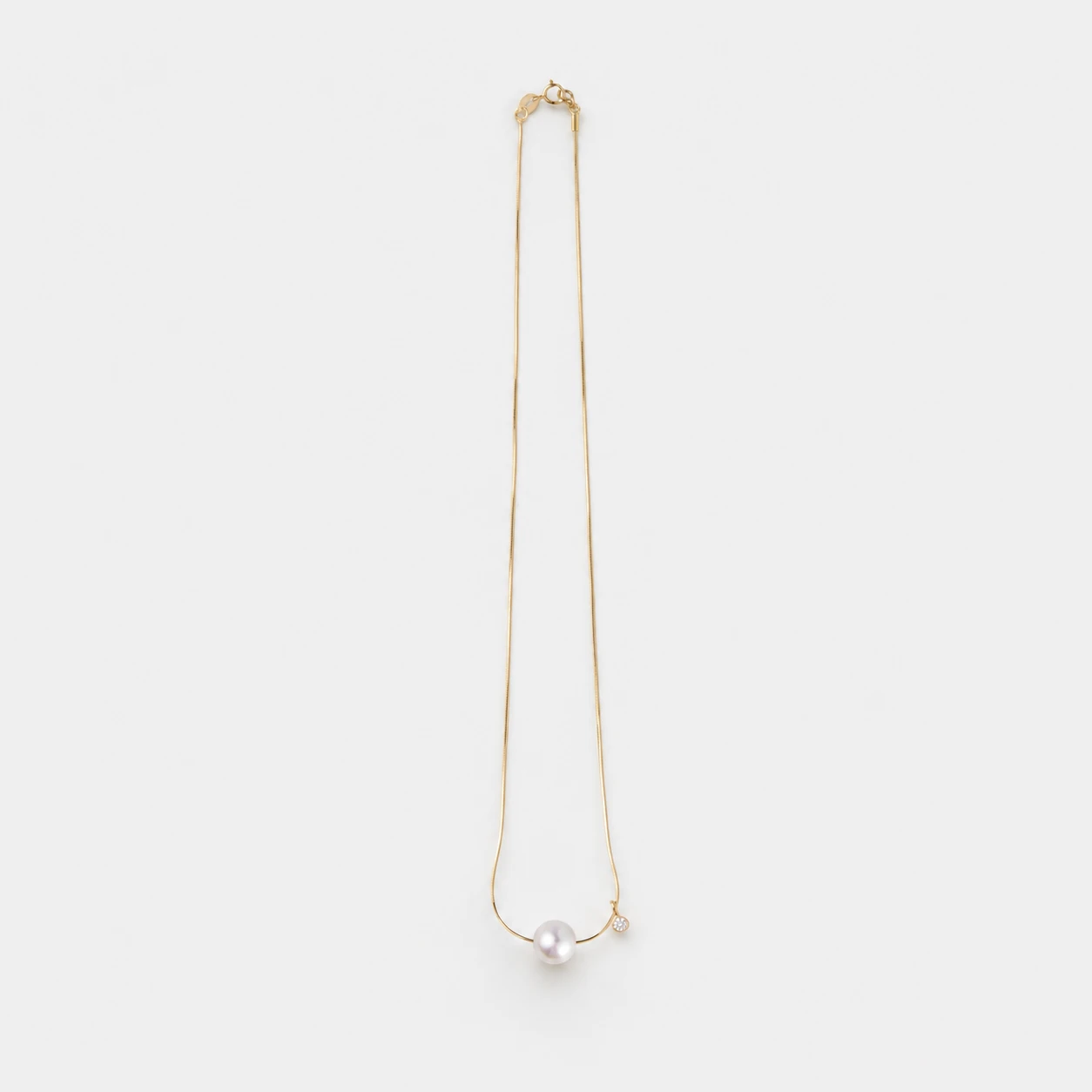 delicate-14k-gold-vermeil-natalia-necklace-with-single-pearl-solitaire An elegant and polished 14K Gold Vermeil necklace with a singular, lustrous white pearl and a tiny sparkling cubic zirconia charm, perfect for achieving a refined, everyday look.