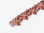 Close-up of ONDA LENTA garnet beaded jewelry with faceted deep-red gemstones, intricate woven metalwork and sculptural silver-tone ring details.