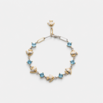 A handcrafted 18K gold plated sterling silver blue topaz bracelet with alternating square-cut stones and textured two-tone fan charms, providing a distinctive coastal look.