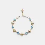 A handcrafted 18K gold plated sterling silver blue topaz bracelet with alternating square-cut stones and textured two-tone fan charms, providing a distinctive coastal look.