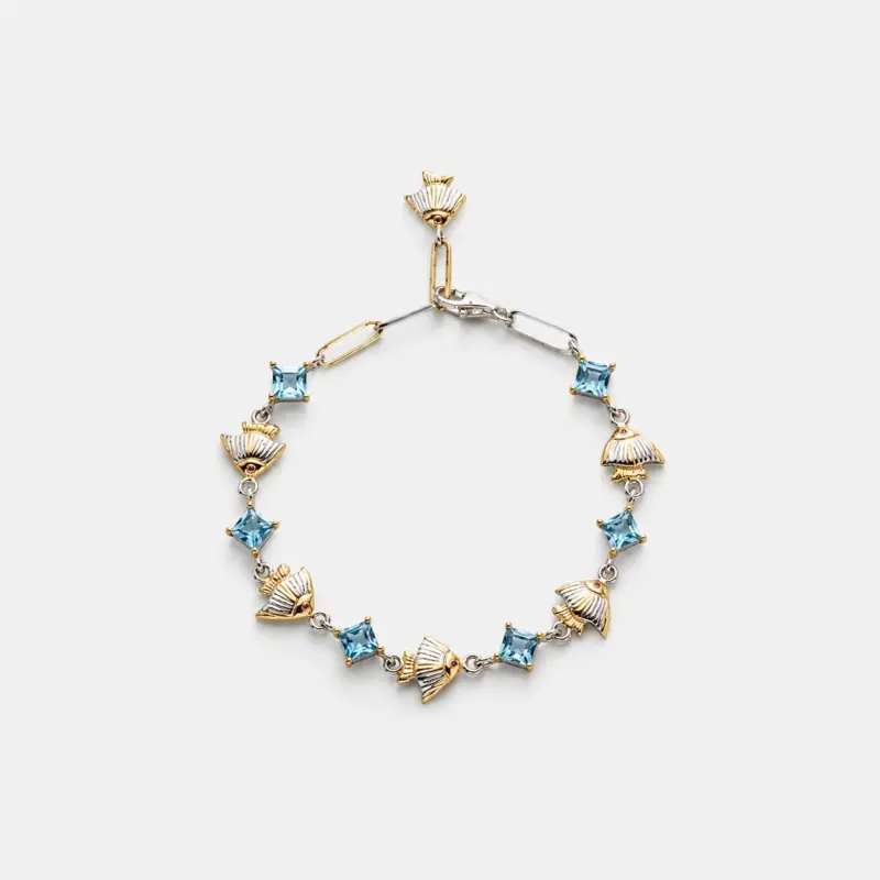A handcrafted 18K gold plated sterling silver blue topaz bracelet with alternating square-cut stones and textured two-tone fan charms, providing a distinctive coastal look.