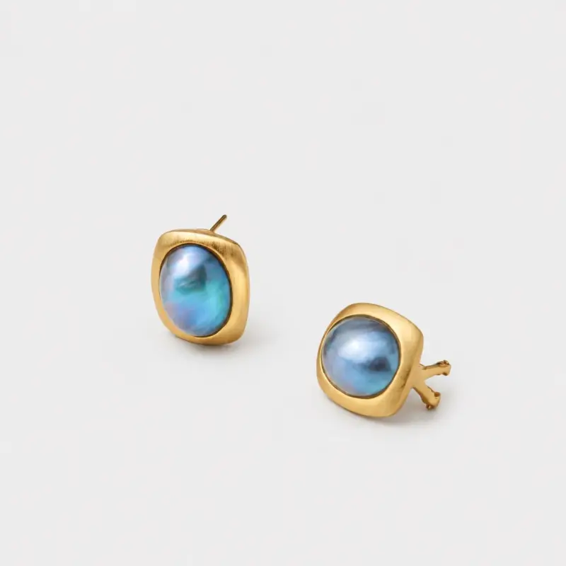 Angled close-up view of the pair of iridescent mabe pearl stud earrings in rounded square gold frames, displaying the secure post and clutch back mechanism