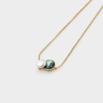 Perspective view showing the detailed iridescent green abalone shell pattern alongside a smooth round pearl on a fine gold plated link chain.
