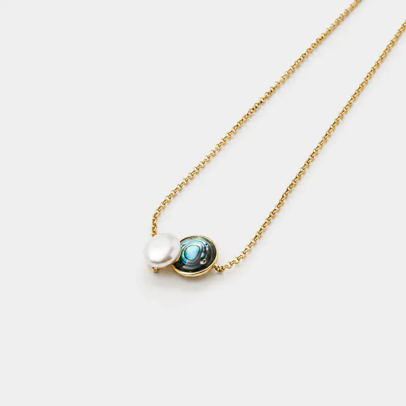 Perspective view showing the detailed iridescent green abalone shell pattern alongside a smooth round pearl on a fine gold plated link chain.