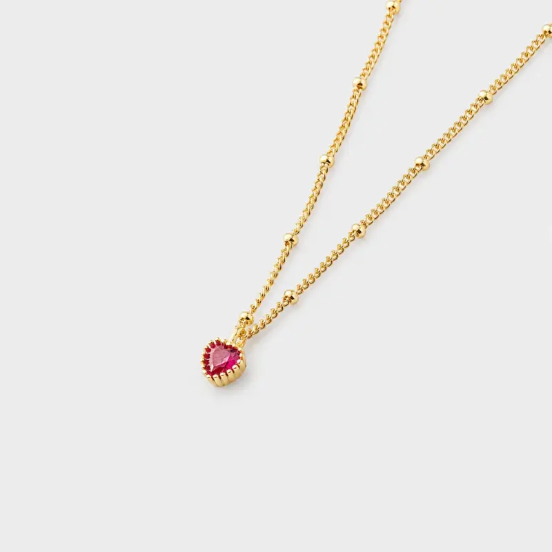 Perspective view showing textured gold bead accents and a faceted red heart pendant necklace in 18K gold plated sterling silver.