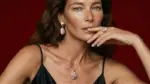 Model wearing ONDA LENTA pink baroque pearl drop earrings, a matching pearl pendant necklace and a delicate pearl ring against a deep red background.