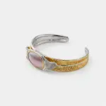 Side detail view showing the textured, feather-like silver and gold shanks framing an oval pink mabe pearl in a secure gold bezel.