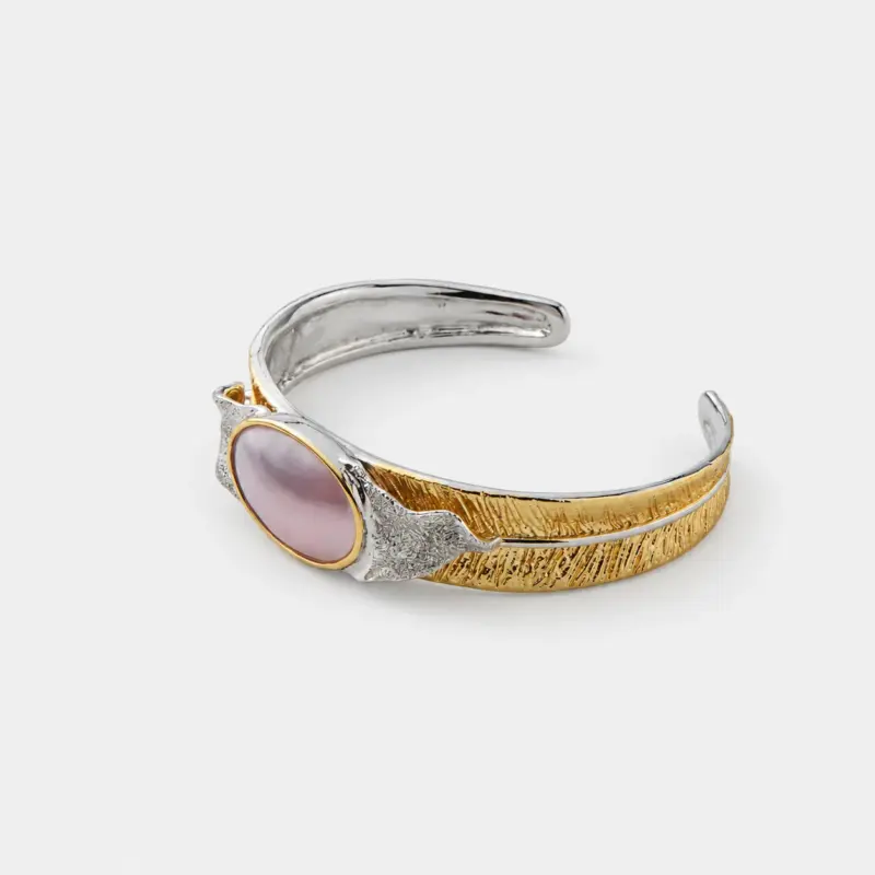 Side detail view showing the textured, feather-like silver and gold shanks framing an oval pink mabe pearl in a secure gold bezel.