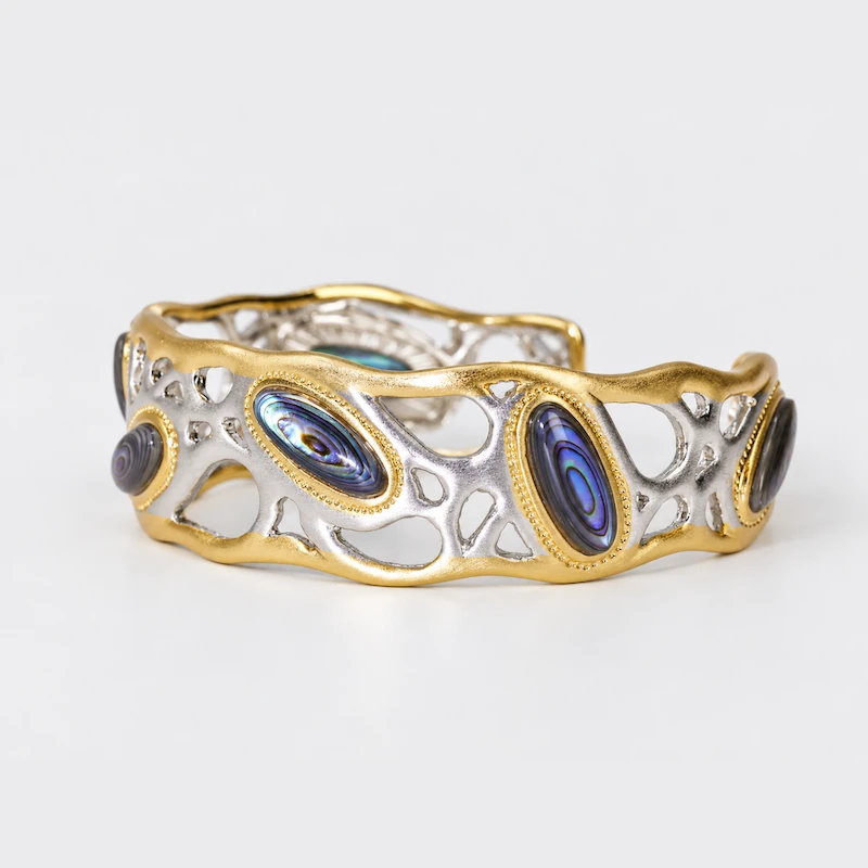 Front view of an ONDA LENTA wide cuff bracelet featuring natural abalone shell inlays and an organic two-tone openwork design.