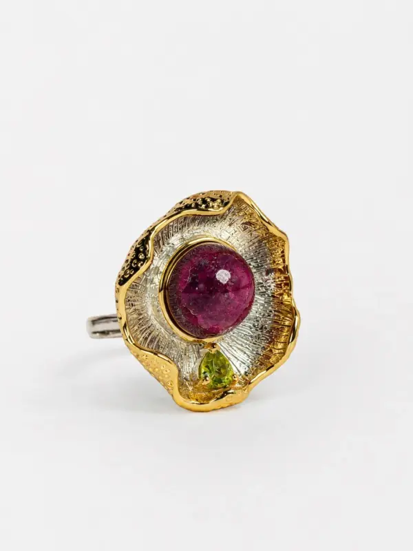 Side perspective of the pendant showcasing the textured radiating metalwork and the vibrant contrast between the ruby center and peridot accent