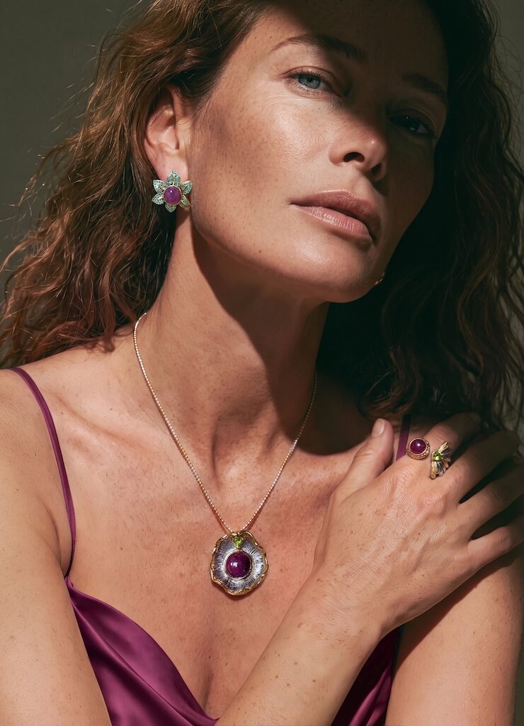 Model wearing ONDA LENTA luxury jewelry set, featuring a wavy organic pendant necklace with a large purple cabochon gemstone, matching flower stud earrings, and a cocktail ring under dramatic cinematic sunlight