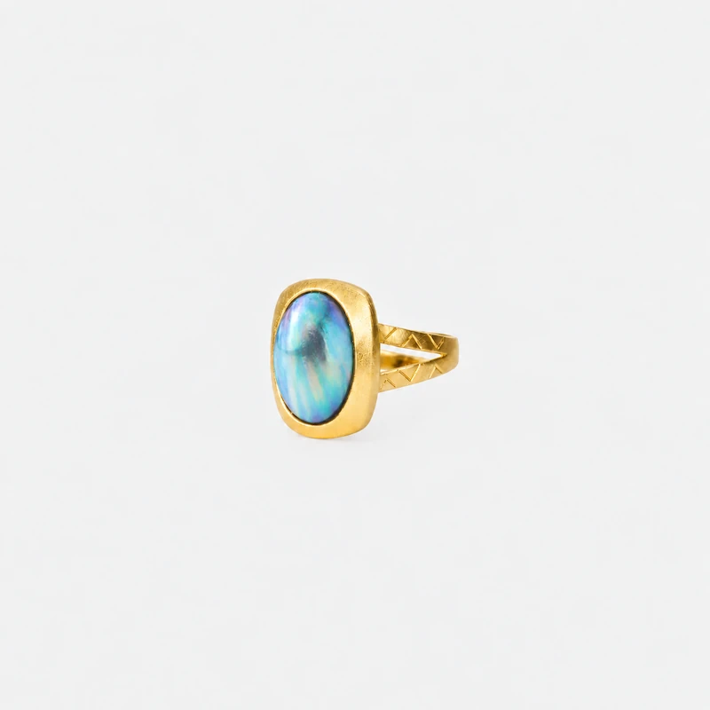 ONDA LENTA gold statement ring featuring an oval iridescent blue-green gemstone with a textured geometric split band.