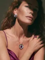 Model wearing ONDA LENTA luxury jewelry set, featuring a wavy organic pendant necklace with a large purple cabochon gemstone, matching flower stud earrings, and a cocktail ring under dramatic cinematic sunlight
